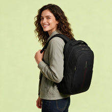 Load image into Gallery viewer, A woman with curly brown hair smiling and posing from the side, wearing a black backpack with a red accent stripe on a light green studio background.
